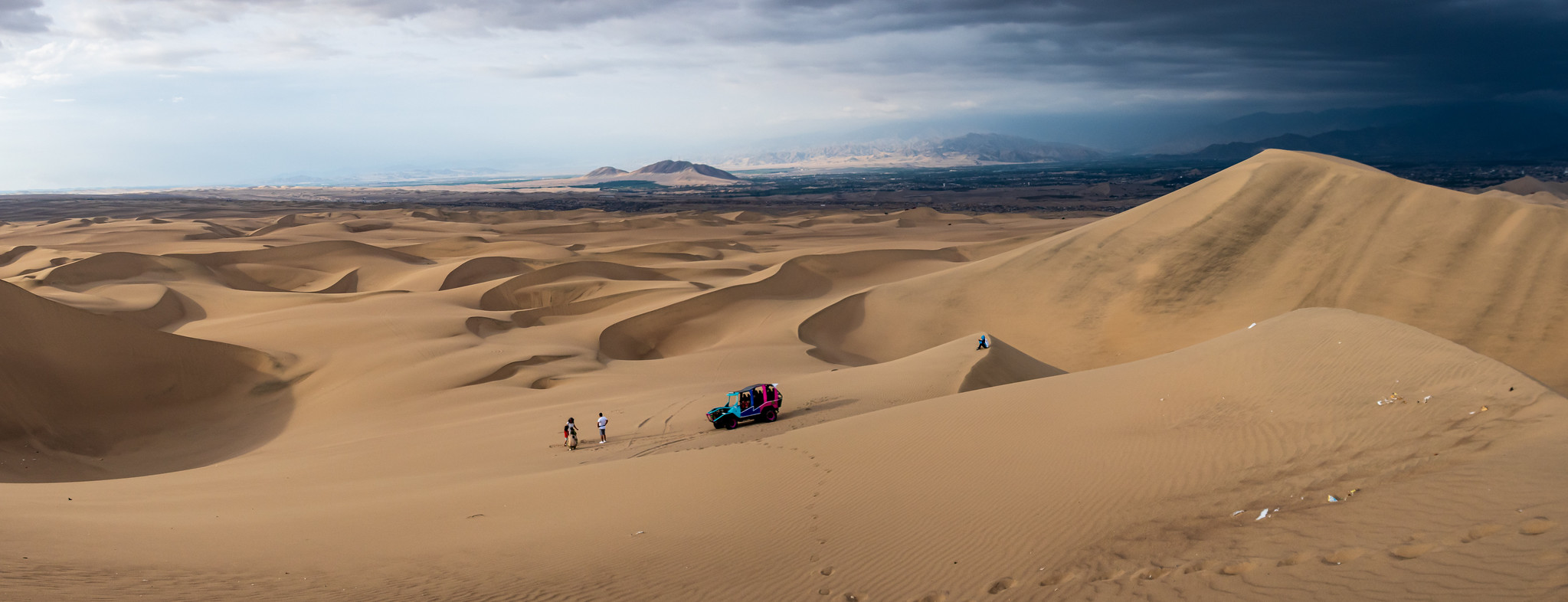 Dune buggy and travelers surrounded by broad Huacachina dunes